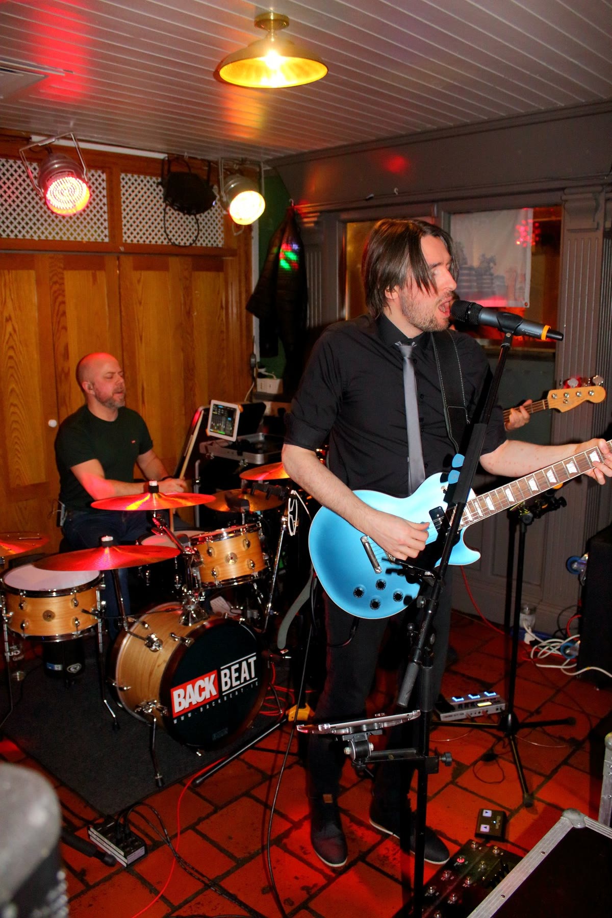 A singer with a blue guitar and a drummer behind him