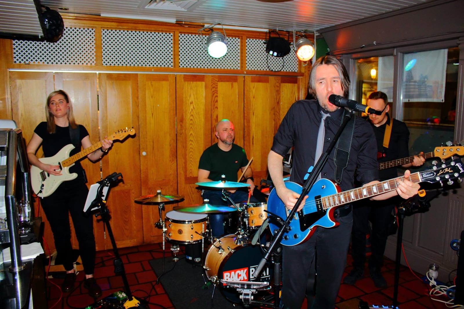 A band playing guitar and drums in the corner of the lounge