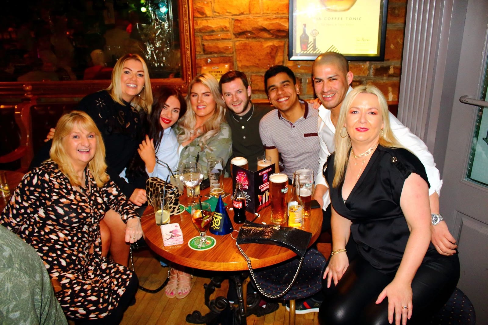 Friends crowded round a corner table in the bar, smiling at the camera