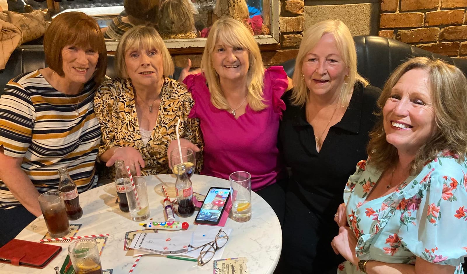 Five women laughing at a round table with drinks and bingo books